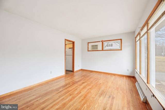 empty room featuring a baseboard heating unit, baseboards, and light wood-style floors