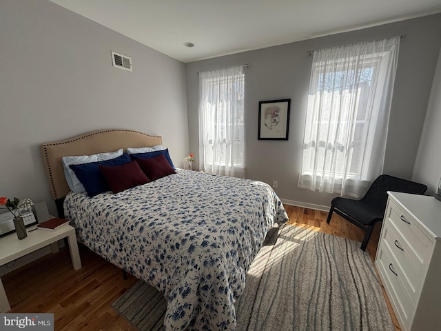 bedroom with wood finished floors, baseboards, multiple windows, and visible vents