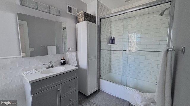 bathroom with tile walls, visible vents, shower / bath combination with glass door, and vanity