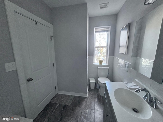bathroom featuring tile walls, visible vents, toilet, vanity, and wainscoting