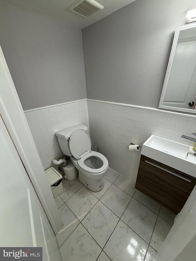 half bathroom with tile walls, a wainscoted wall, visible vents, marble finish floor, and toilet