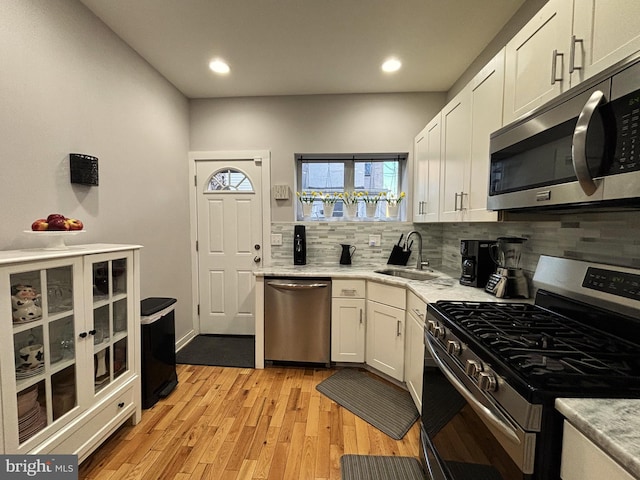 kitchen featuring a sink, light wood finished floors, appliances with stainless steel finishes, white cabinets, and decorative backsplash