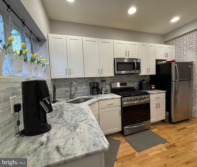 kitchen with light wood-style flooring, decorative backsplash, a sink, and stainless steel appliances