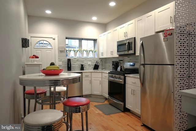 kitchen featuring white cabinetry, stainless steel appliances, light wood-style floors, decorative backsplash, and recessed lighting