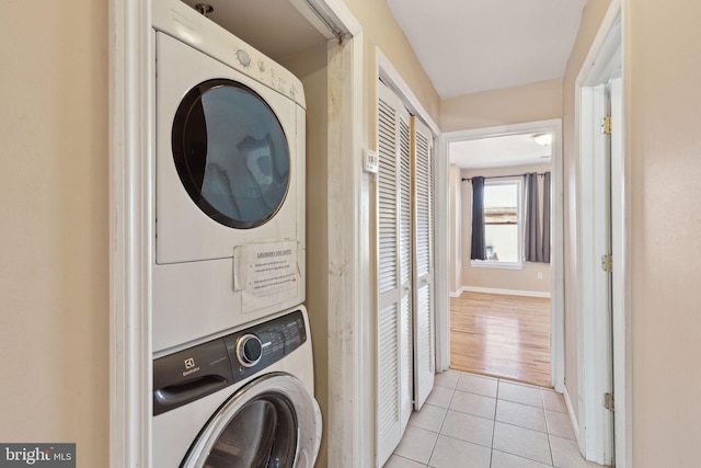 laundry area featuring stacked washer and dryer, laundry area, baseboards, and light tile patterned floors