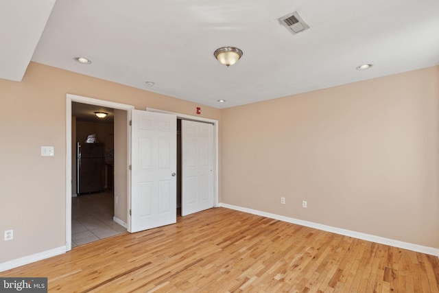 unfurnished bedroom featuring freestanding refrigerator, baseboards, visible vents, and light wood finished floors