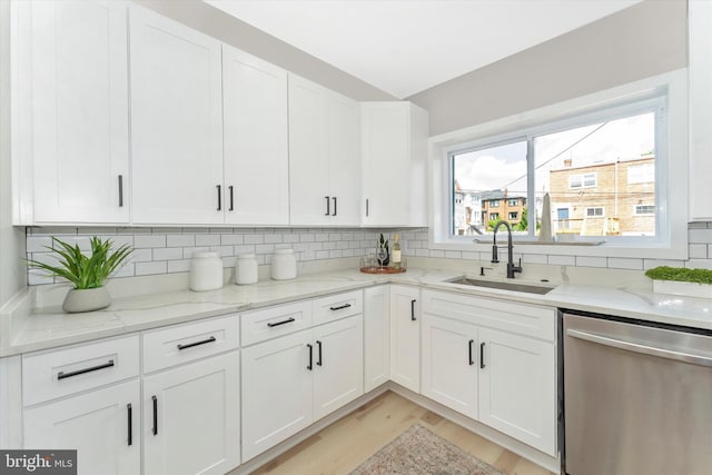 kitchen with stainless steel dishwasher, white cabinets, backsplash, and a sink