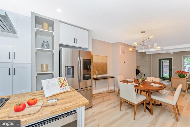 kitchen featuring light wood finished floors, stainless steel fridge with ice dispenser, white cabinets, wall chimney range hood, and a chandelier