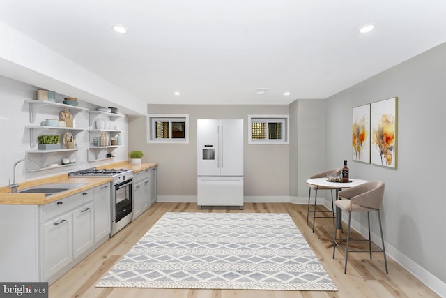 kitchen with light wood finished floors, open shelves, a sink, white fridge with ice dispenser, and stainless steel gas stove