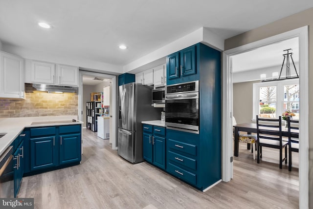 kitchen with appliances with stainless steel finishes, blue cabinets, light wood-type flooring, white cabinetry, and backsplash