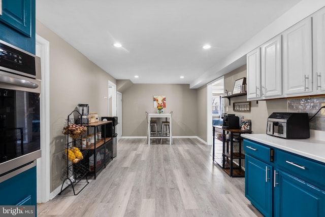 kitchen with white cabinets, blue cabinets, light countertops, light wood-type flooring, and stainless steel oven