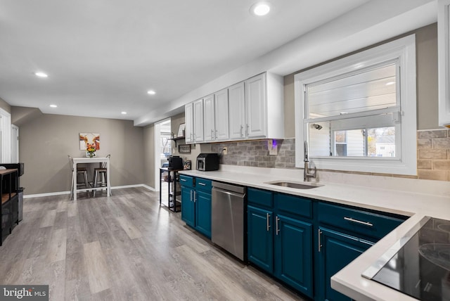 kitchen with blue cabinetry, light countertops, light wood-style flooring, a sink, and dishwasher