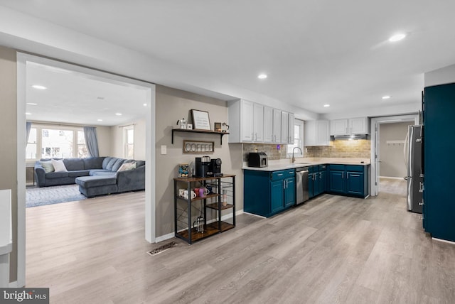 kitchen featuring decorative backsplash, appliances with stainless steel finishes, white cabinets, blue cabinets, and light wood-type flooring