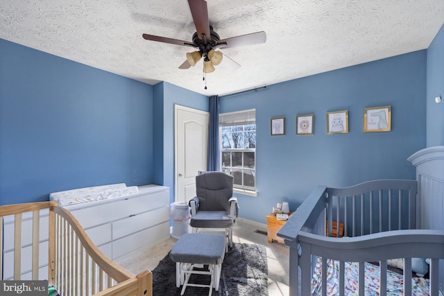 bedroom featuring a textured ceiling, ceiling fan, a nursery area, and carpet