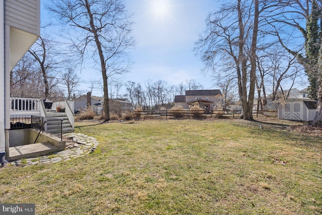 view of yard featuring a storage unit, fence, an outdoor structure, a wooden deck, and stairs