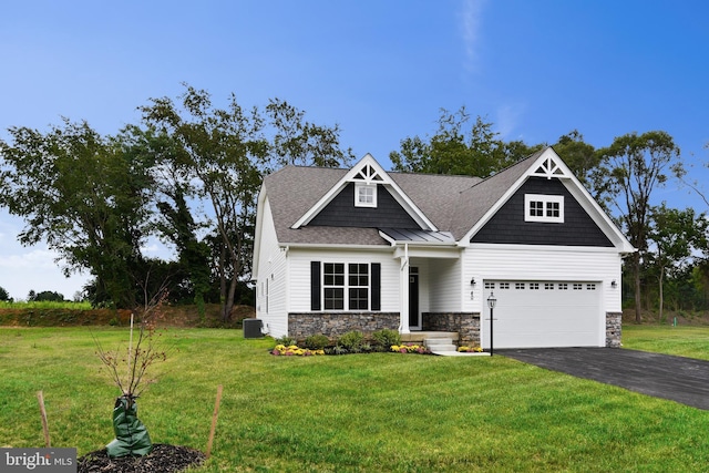 craftsman-style home featuring a shingled roof, a front yard, cooling unit, stone siding, and driveway