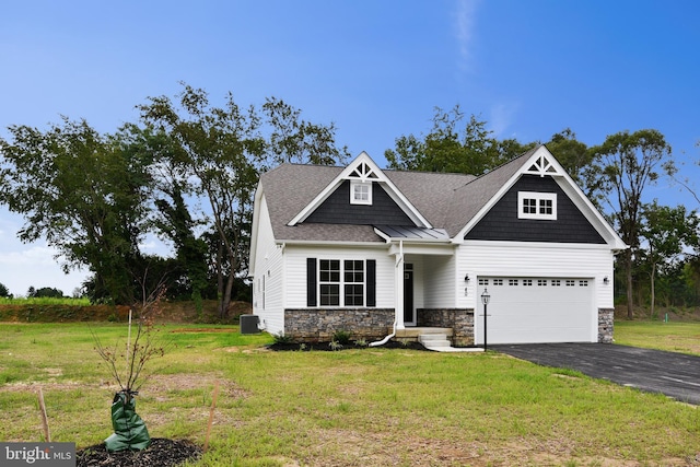 craftsman inspired home with roof with shingles, central air condition unit, a front yard, stone siding, and driveway