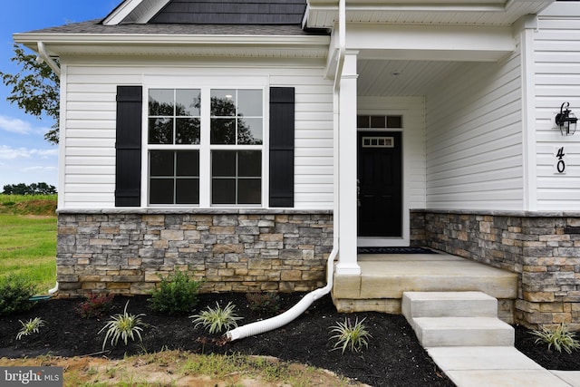 view of exterior entry featuring stone siding and roof with shingles