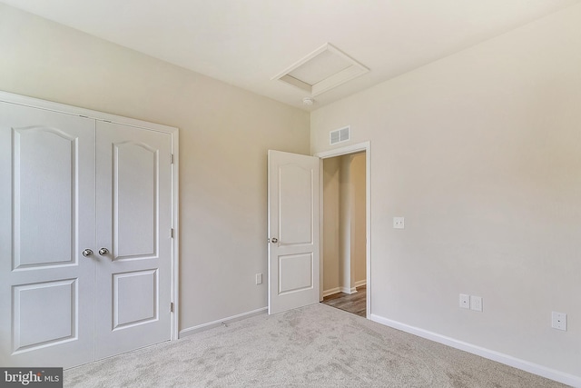 unfurnished bedroom featuring light carpet, attic access, visible vents, and baseboards