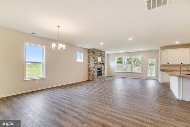 unfurnished living room with a stone fireplace, light wood-style flooring, a sink, and visible vents