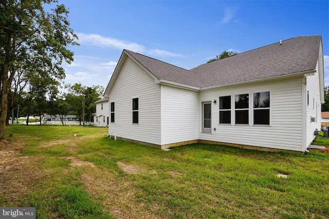 back of house featuring roof with shingles and a lawn