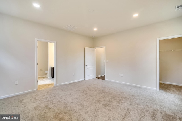 unfurnished bedroom with recessed lighting, a walk in closet, visible vents, and light colored carpet