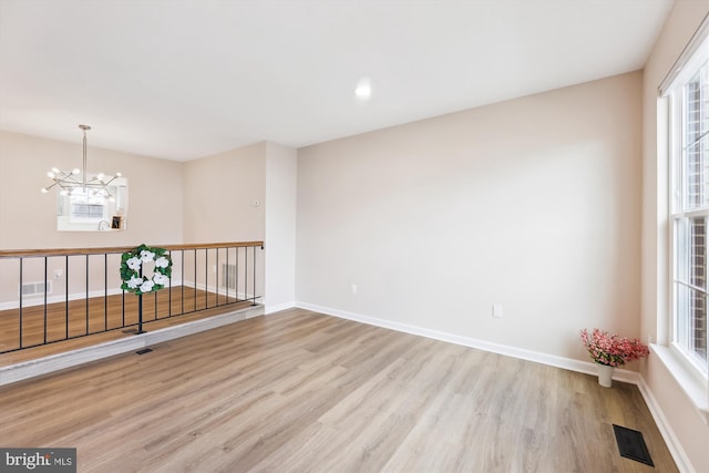 spare room featuring visible vents, plenty of natural light, light wood-style flooring, and an inviting chandelier