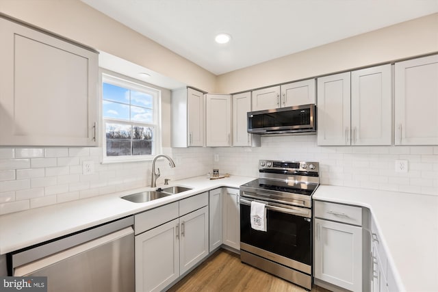 kitchen with backsplash, stainless steel appliances, a sink, and light countertops