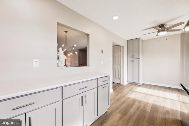 kitchen with gray cabinetry, ceiling fan with notable chandelier, baseboards, light countertops, and light wood-type flooring