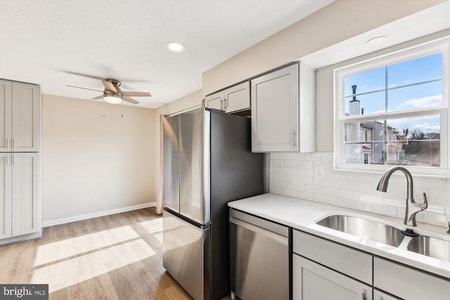 kitchen featuring a sink, light wood-style floors, light countertops, appliances with stainless steel finishes, and tasteful backsplash