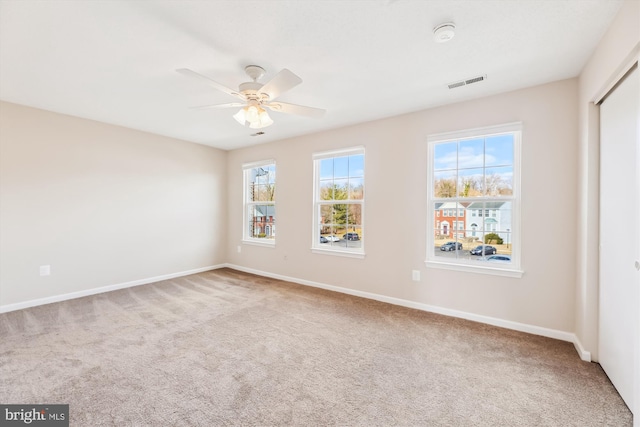 carpeted spare room with ceiling fan, visible vents, and baseboards