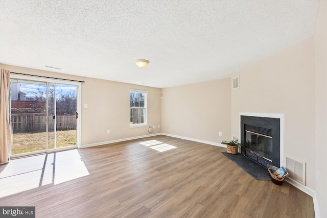 unfurnished living room with a textured ceiling, wood finished floors, a glass covered fireplace, and visible vents