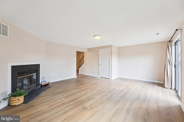 unfurnished living room with visible vents, a glass covered fireplace, light wood-type flooring, baseboards, and stairs