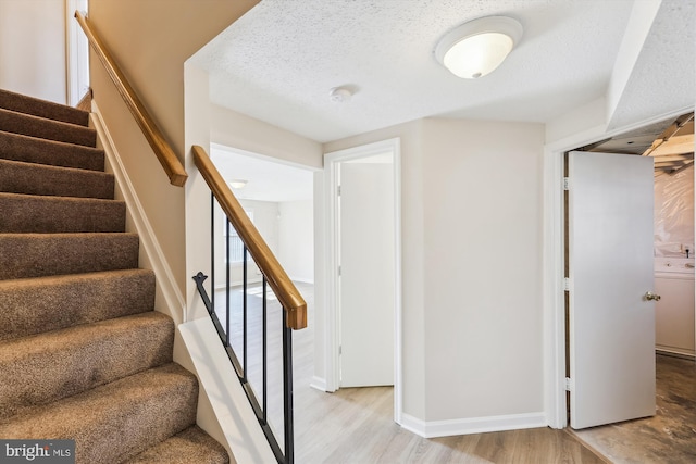 stairs with a textured ceiling, baseboards, and wood finished floors