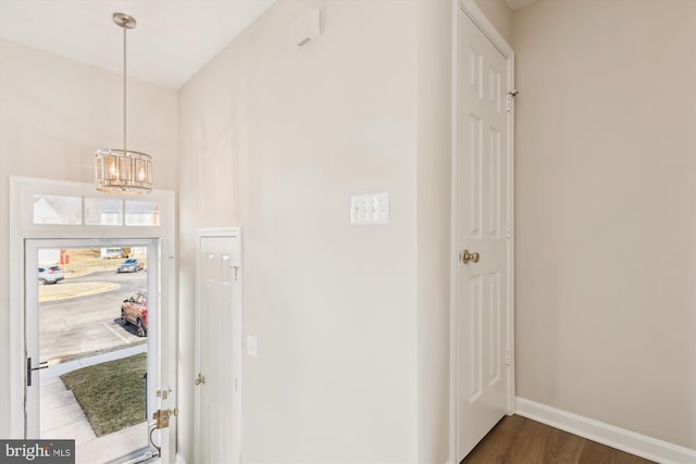 foyer entrance with dark wood-type flooring, a chandelier, and baseboards