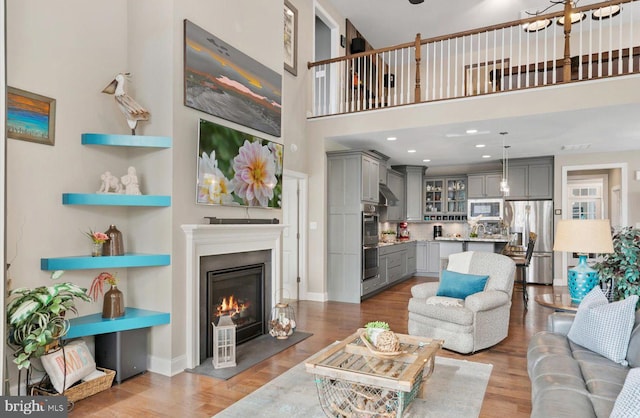 living area with wood finished floors, baseboards, recessed lighting, a towering ceiling, and a glass covered fireplace