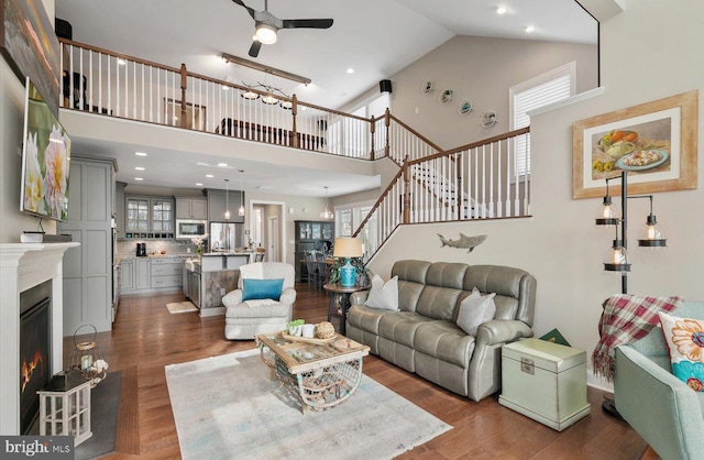 living room featuring a healthy amount of sunlight, stairs, a lit fireplace, and wood finished floors