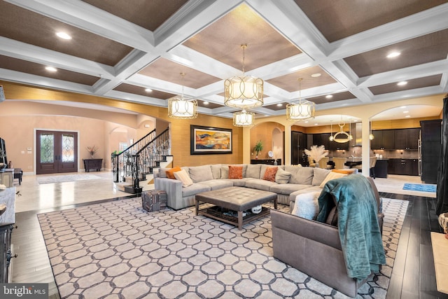 living area featuring arched walkways, stairway, wood finished floors, beamed ceiling, and french doors