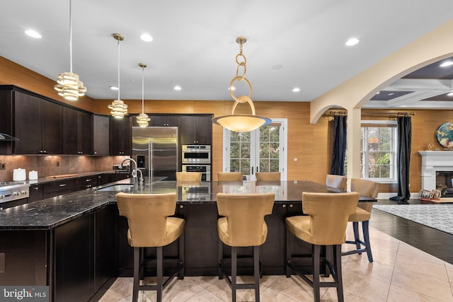 kitchen with arched walkways, stainless steel appliances, backsplash, a sink, and dark stone counters