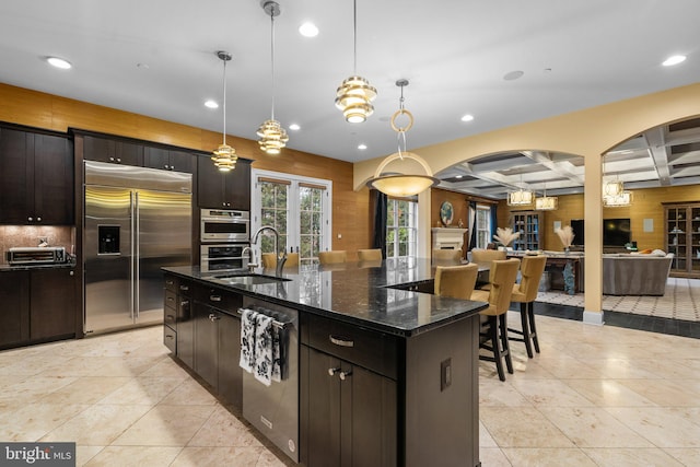 kitchen featuring arched walkways, coffered ceiling, a sink, open floor plan, and appliances with stainless steel finishes