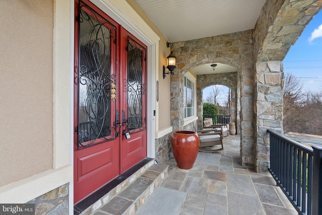 entrance to property featuring covered porch, stone siding, and stucco siding