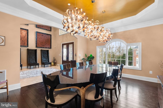 dining area featuring baseboards, a raised ceiling, dark wood-type flooring, crown molding, and a chandelier