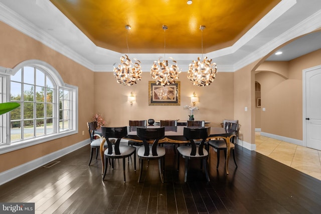 dining room featuring arched walkways, a raised ceiling, ornamental molding, wood finished floors, and baseboards