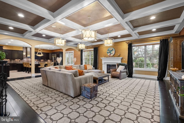 living area featuring a healthy amount of sunlight, arched walkways, beamed ceiling, and a glass covered fireplace