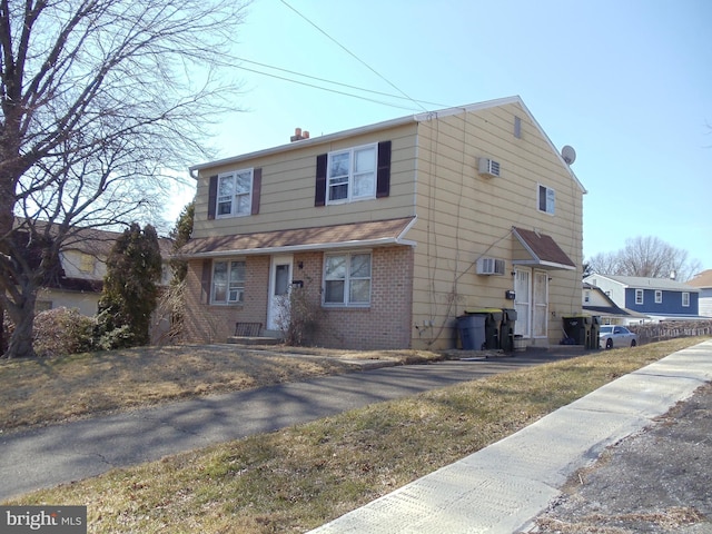 view of front of house with brick siding, a wall unit AC, and a chimney