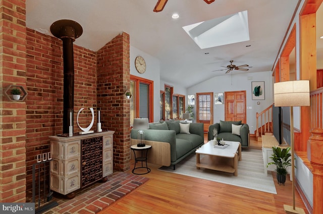 living area featuring lofted ceiling with skylight, a wood stove, ceiling fan, and wood finished floors