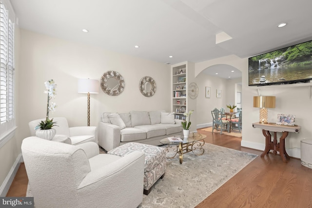 living room featuring arched walkways, baseboards, recessed lighting, and wood finished floors