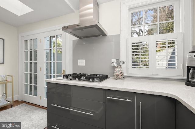 kitchen featuring a skylight, dark cabinets, light countertops, stainless steel gas cooktop, and exhaust hood