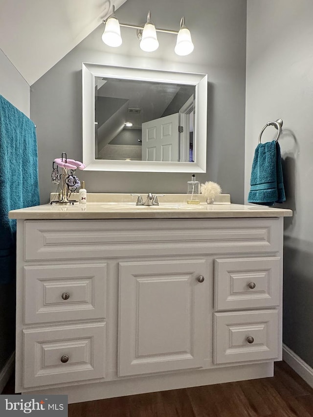 bathroom with baseboards, wood finished floors, vanity, and vaulted ceiling