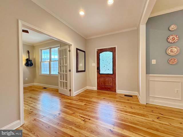 entrance foyer featuring visible vents, a wainscoted wall, ornamental molding, and light wood finished floors